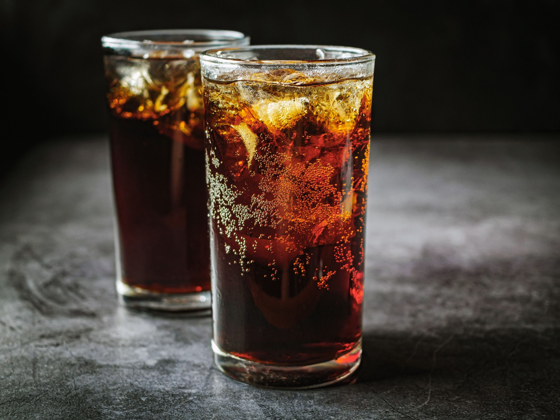 Cola soft drink with ice cubes, soda fizzy drink in Cold two glass on gray background