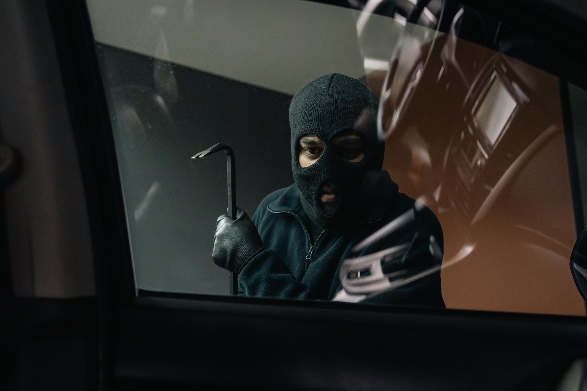 Thief in uniform black jacket various action stolen cars. The Robber terrorism criminal car with balaclava and crowbar breaking into a car window